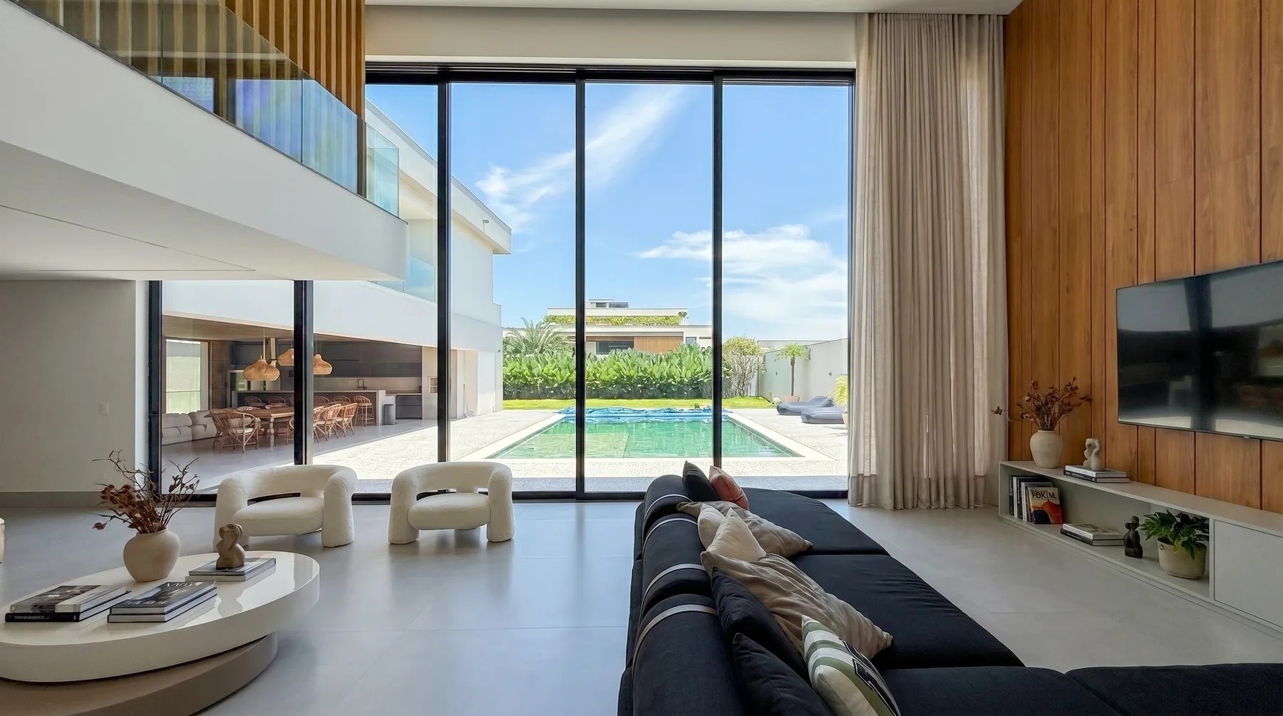 Living de pé-direito duplo em residência de alto padrão com marcenaria integrada e vista para a piscina, projeto no Rio de Janeiro